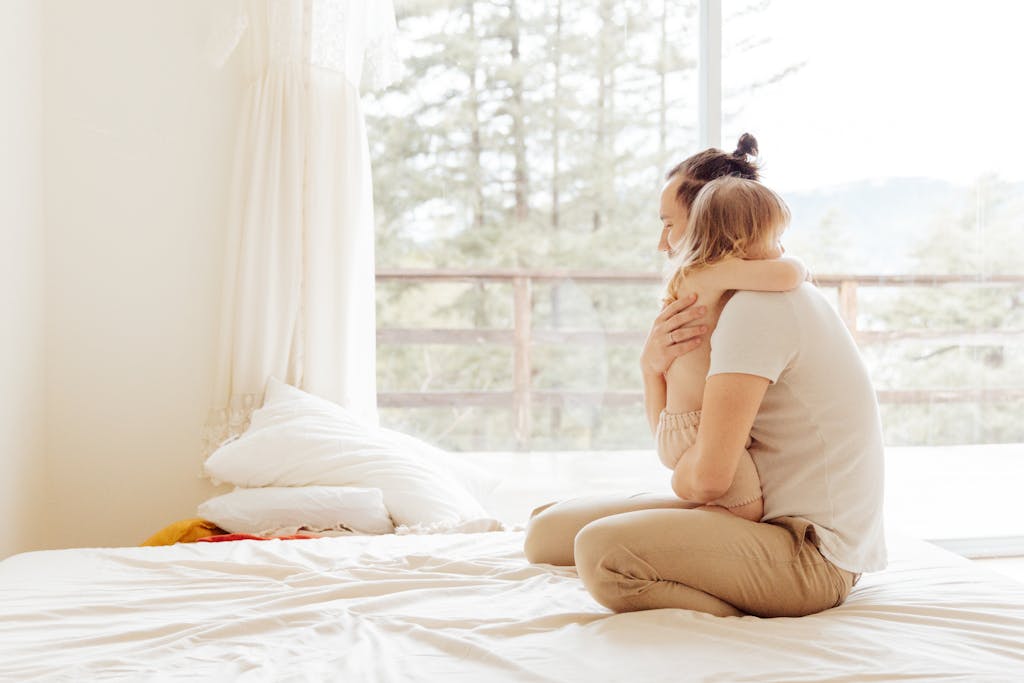 A loving father embraces his child on a cozy bed in a warmly lit bedroom.